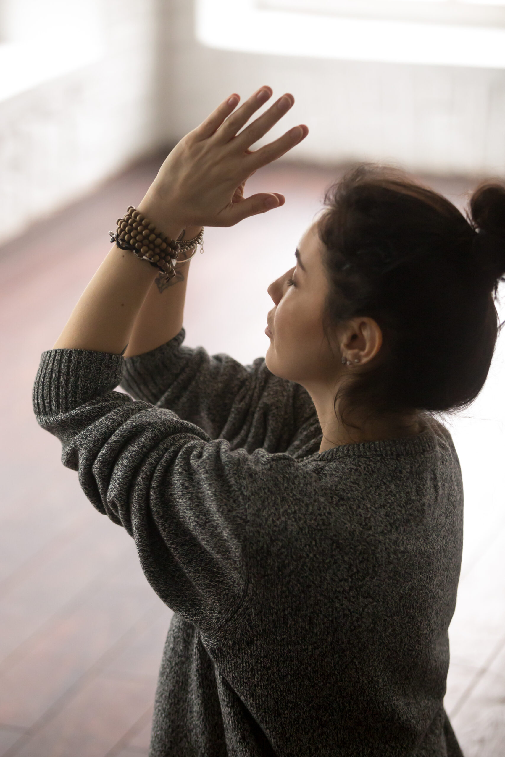 young attractive woman in grey sweater making namaste, loft stud